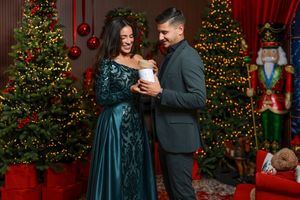 Elegant couple in formal wear celebrating Christmas, surrounded by decorated trees, lights, and nutcracker decorations.