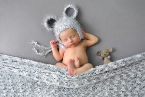 Baby portrait wearing gray mouse ears lying on patterned bedding.