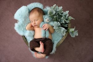 Newborn photography on teal blanket with decorative greenery.