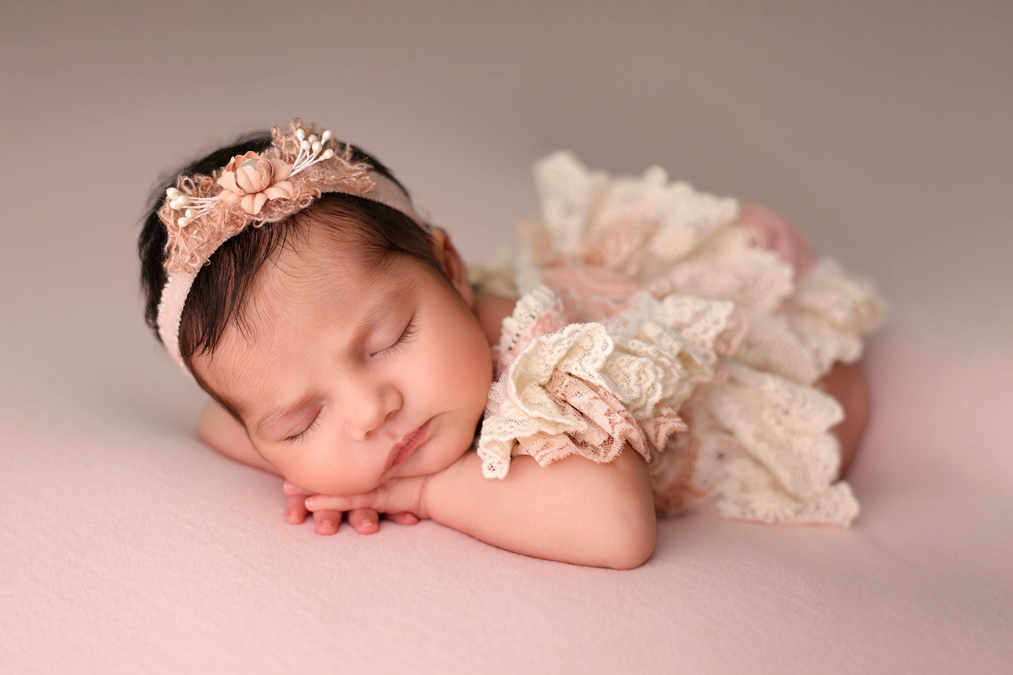 Delicate newborn photography series featuring peaceful sleeping baby in soft pink and cream tones.