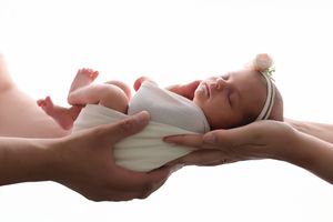 Newborn baby sleeping peacefully in parents hands against white background.