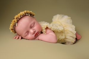 Sleeping newborn wearing yellow headpiece and cream tulle wrap during professional photoshoot.
