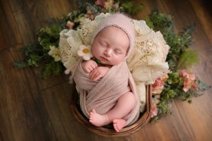 Professional newborn photography with vintage lace and floral accents on wooden backdrop.