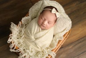 Newborn wrapped in cream knit blanket sleeping peacefully in wooden basket.