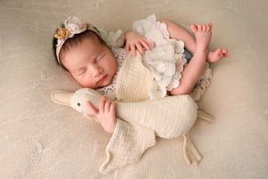 Peacefully sleeping infant in cream knit outfit cuddling with white plush bunny toy on soft textured backdrop.