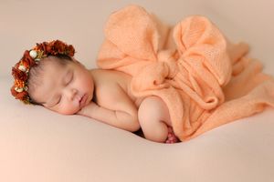 Artistic newborn portrait series with peach-colored fabric and floral accessories.