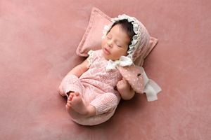 Infant wrapped in pink lace fabric lying on soft pink backdrop during professional newborn photoshoot.