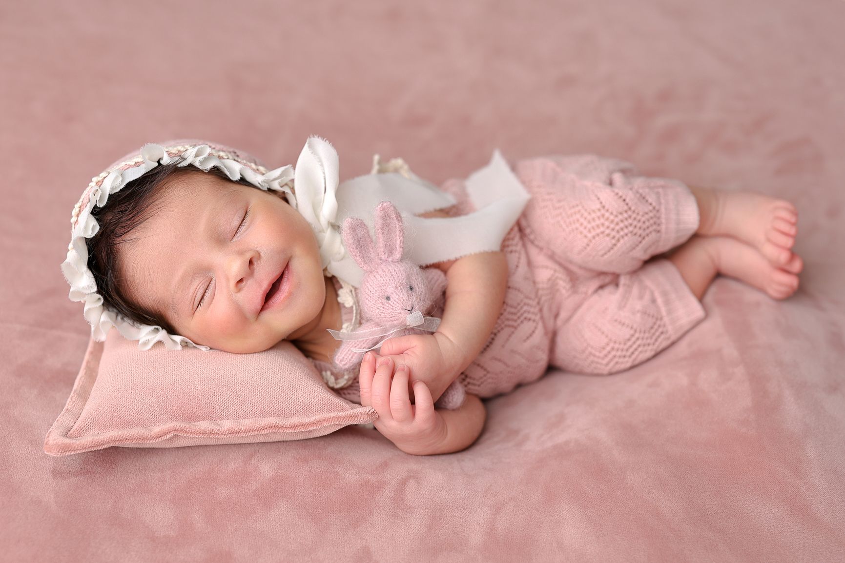 Sleeping baby in pale pink outfit resting on blush colored blanket during portrait session.