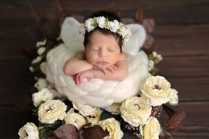 Peaceful newborn nestled among white roses and floral arrangements on dark wooden surface.