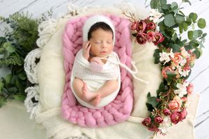 Artistic newborn photography featuring baby surrounded by pink wool decor and floral elements.
