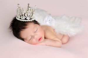 Delicate newborn portrait with soft white fabric and dreamy lighting against pale background.