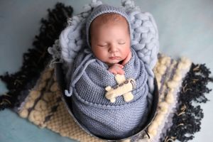 Sleeping baby in gray knit outfit with wooden toy accessory in cozy basket setting.