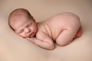 Peaceful sleeping newborn curled up on beige backdrop in artistic nude pose.