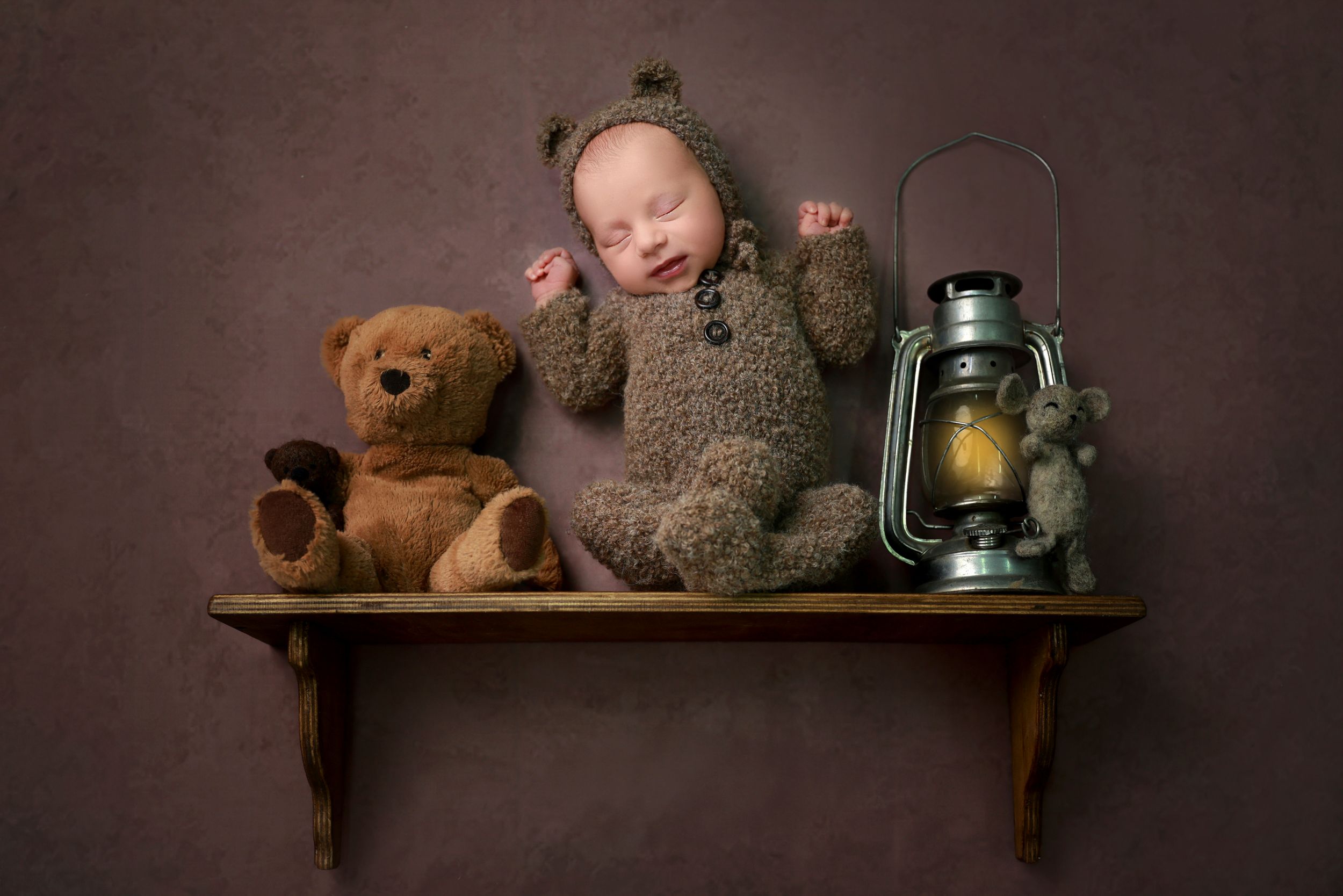 Rustic newborn photography setup with teddy bears and vintage lantern on wooden shelf.