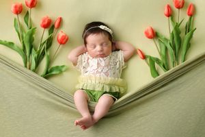 Springtime newborn portrait with orange tulips and green leaves on sage colored backdrop.