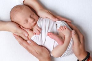 Series of gentle hands holding and supporting newborn baby in white outfit.