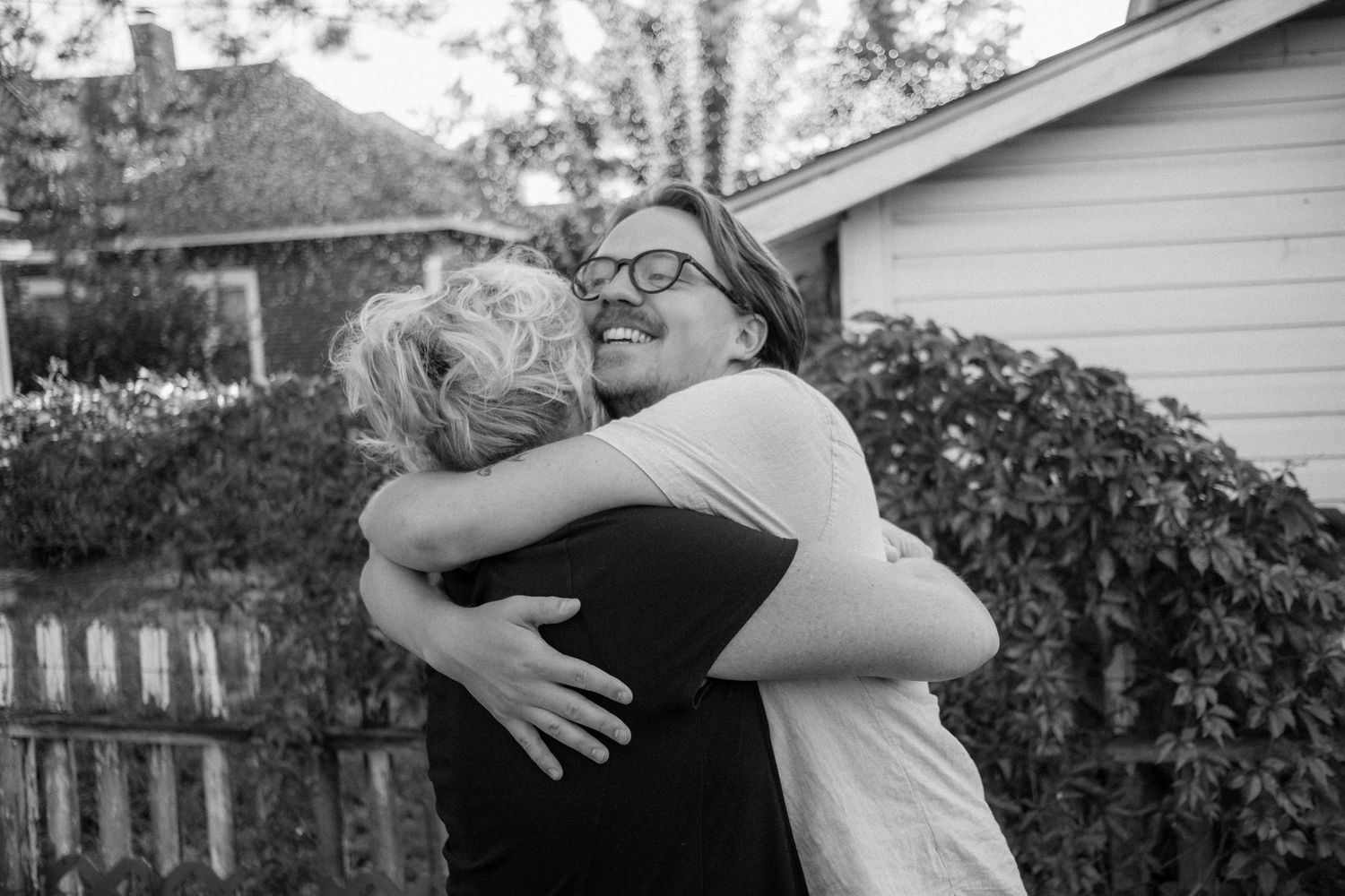 Two people sharing warm embrace in backyard garden setting captured in black and white.