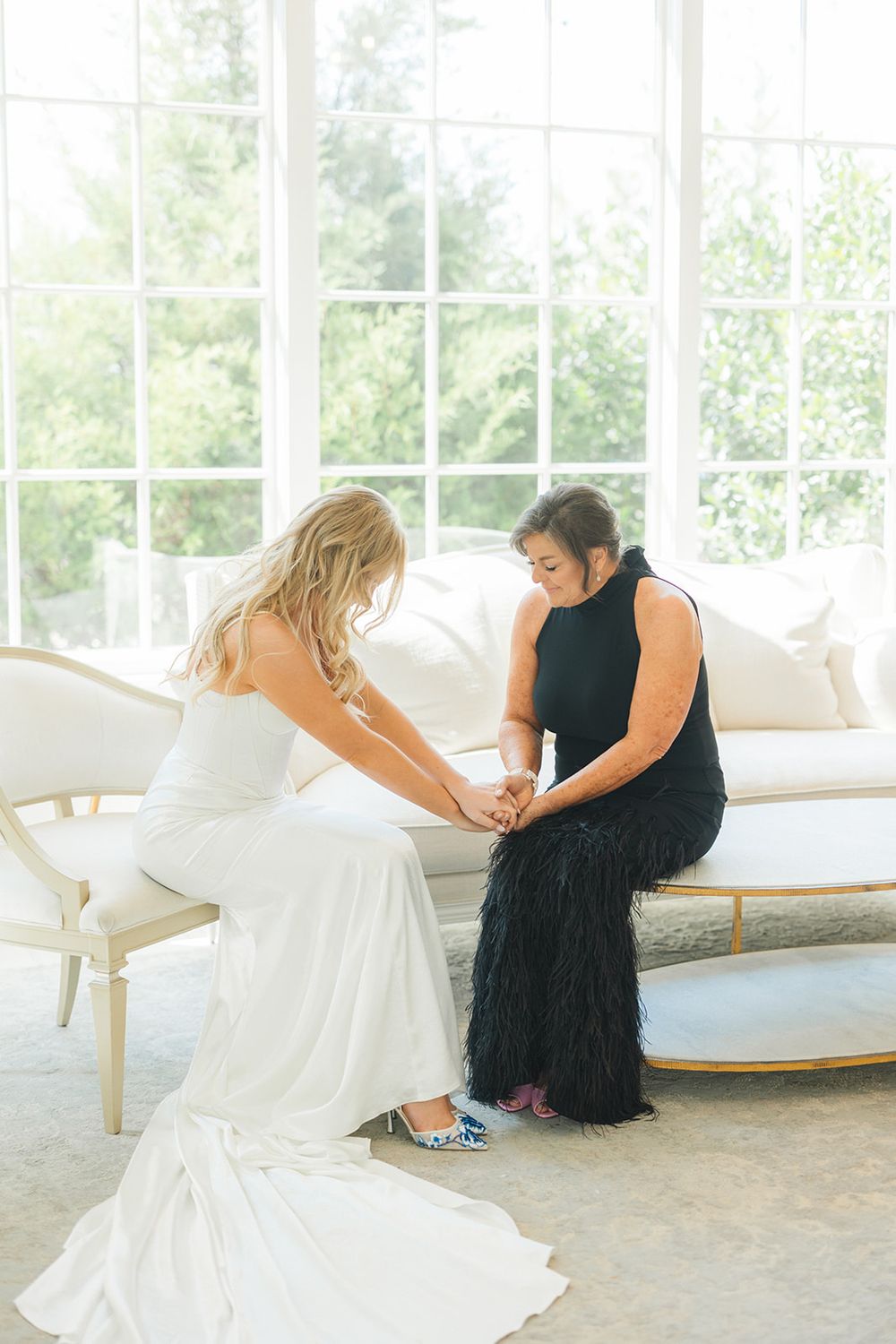 Two people in contrasting white and black formal dresses hold hands while seated in an elegant white room.