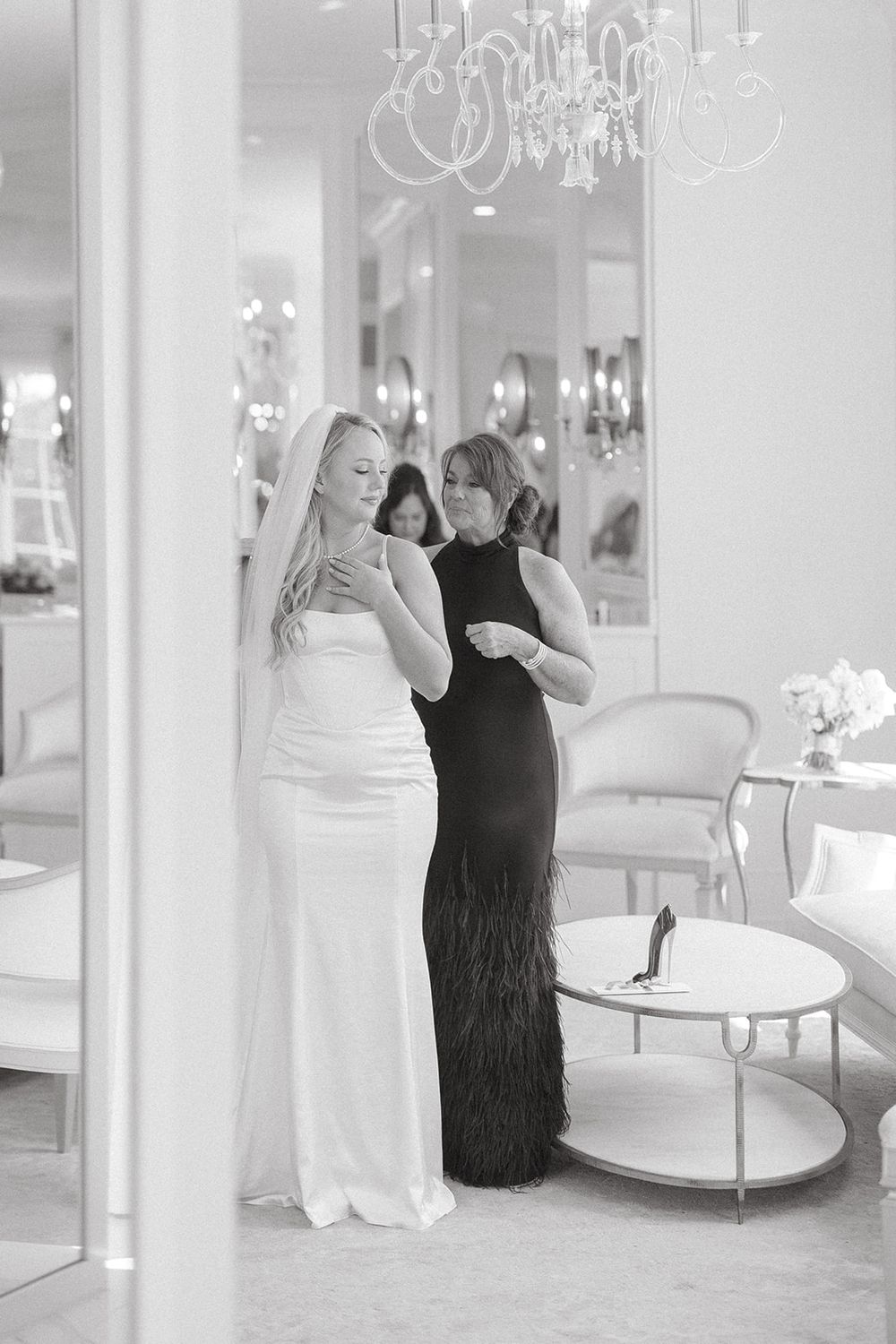 Two figures in black dresses dance together in an elegant white room with mirrors and chandeliers.