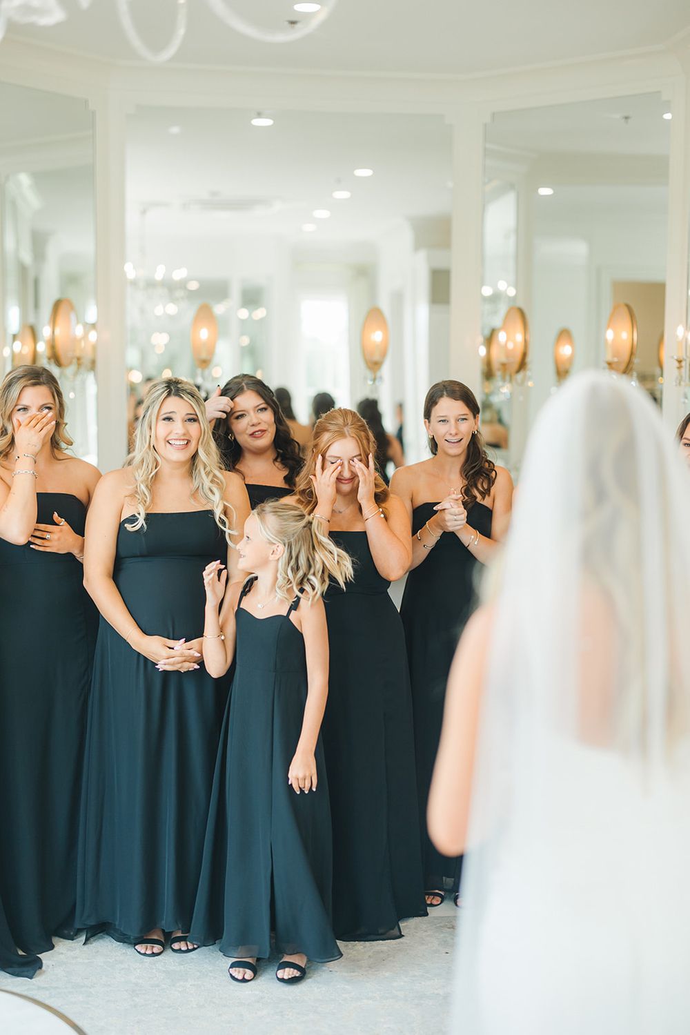 Row of bridesmaids in navy blue dresses react with excitement during wedding day first look reveal.