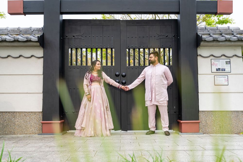 Two people in pink attire hold hands in front of a black ornate gate at an elegant venue entrance.