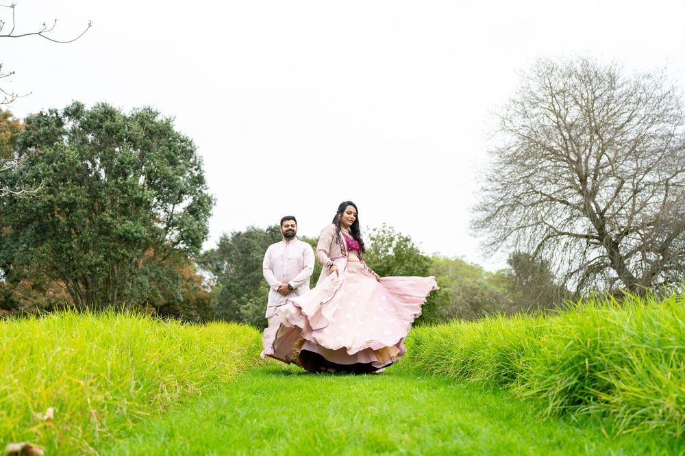A couple in traditional attire twirls together on a lush green hilltop during a spring photoshoot.