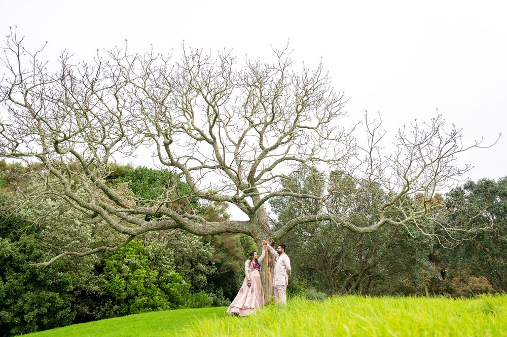 Two figures stand beneath a sprawling bare tree on a grassy hillside during springtime.
