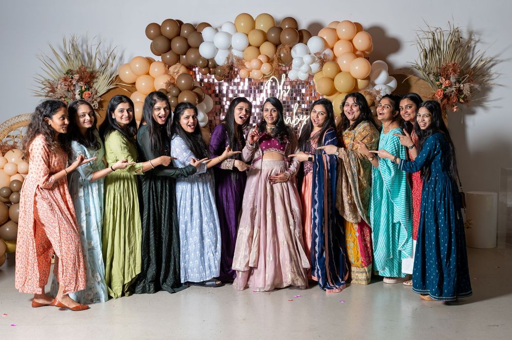 A group wearing colorful floor-length dresses poses together in front of balloon and wheat stalk decorations.