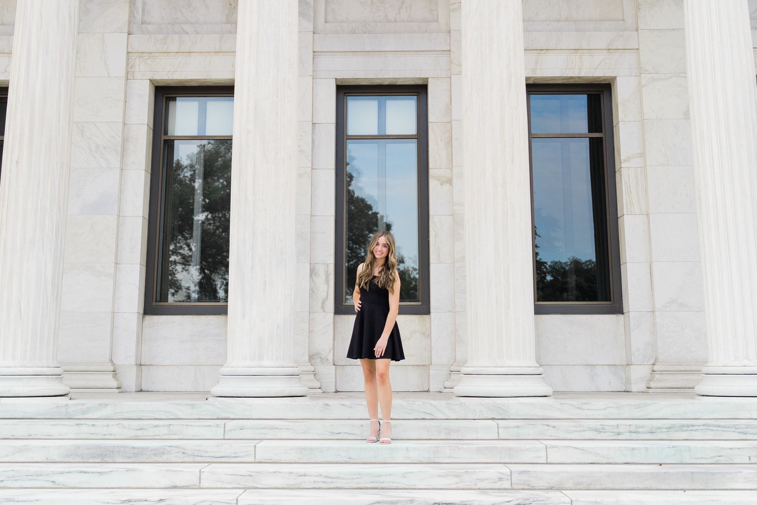 Woman in business attire stands between white marble columns of a grand building entrance.