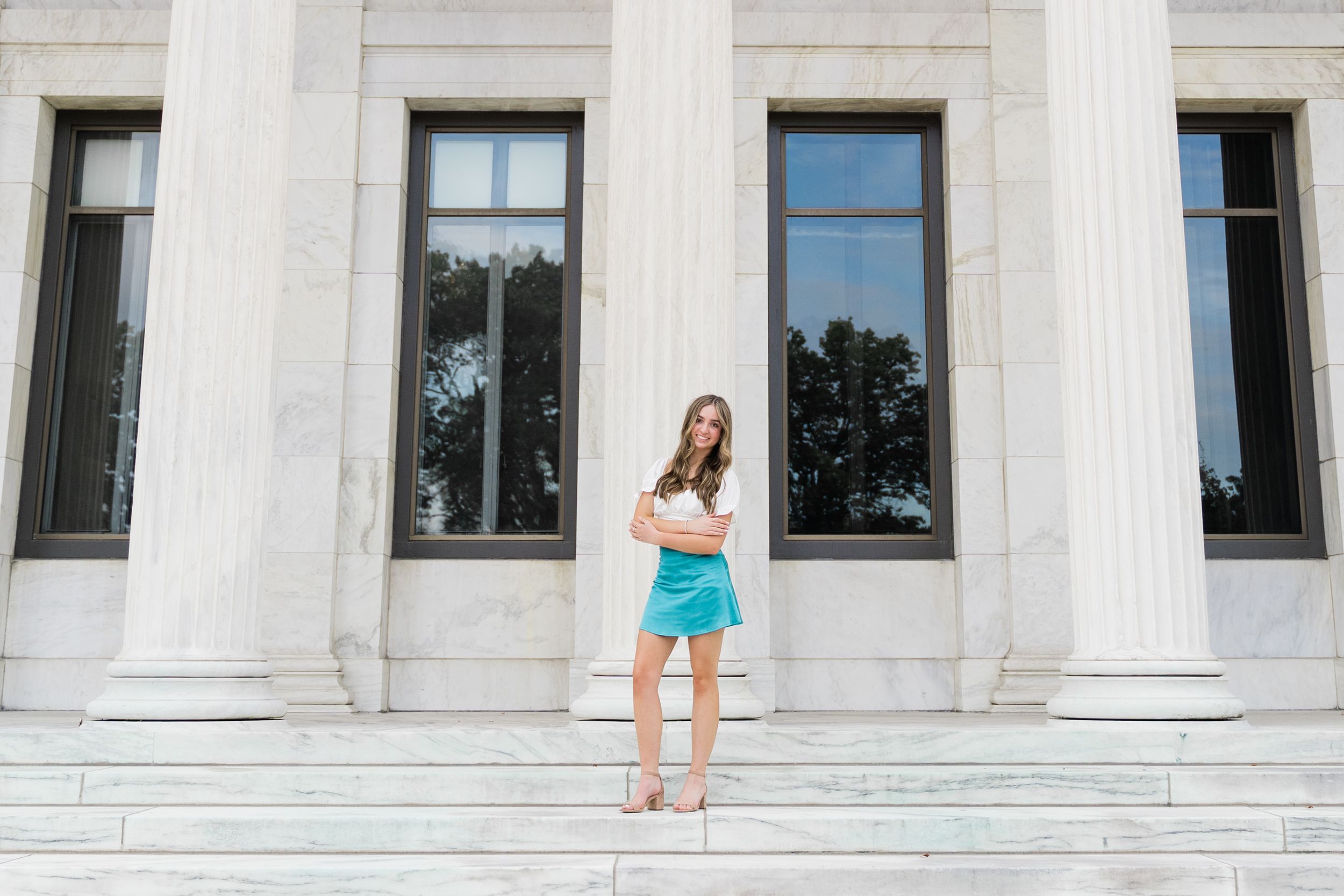 A person in a green dress and heels stands on marble steps in front of a white columned building.
