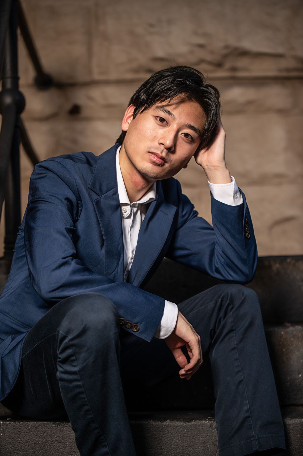 A person in a navy blue suit sits thoughtfully on concrete steps in multiple artistic poses against a textured background.