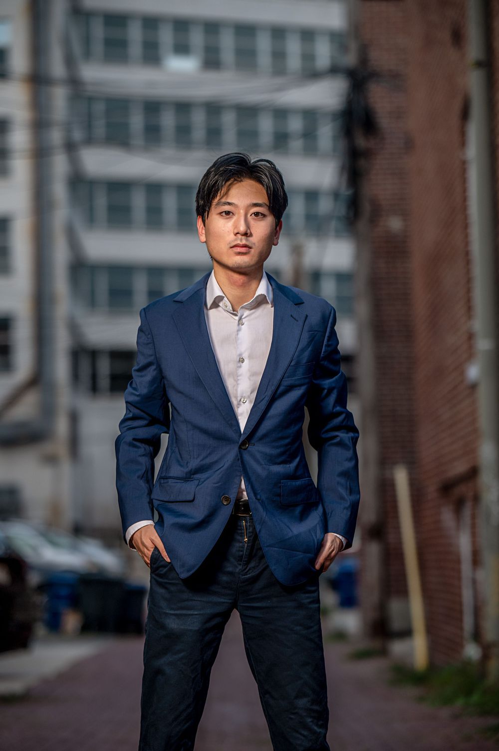 Professional portrait of a person in a navy blazer and white shirt standing confidently in an urban setting.