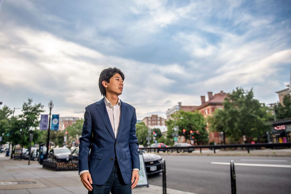 Person in a navy suit walks confidently through an urban area under a dramatic cloudy sky.