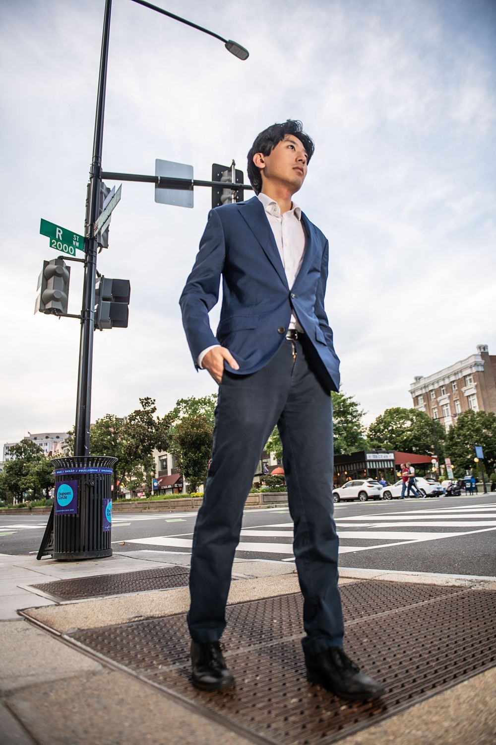 Professional in a navy suit stands confidently at an urban street corner intersection with traffic light and buildings.