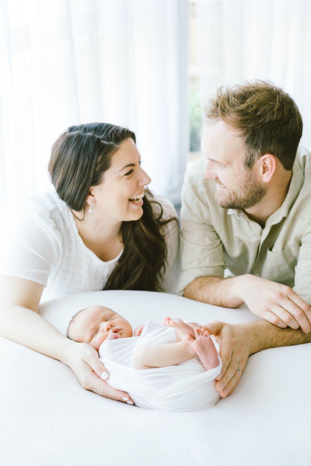 Happy couple looking at each other while their newborn rests between them.