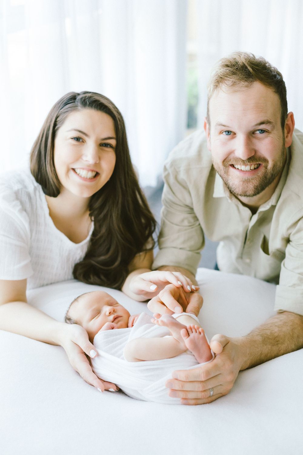 Happy family portrait with newborn baby in bright white setting.