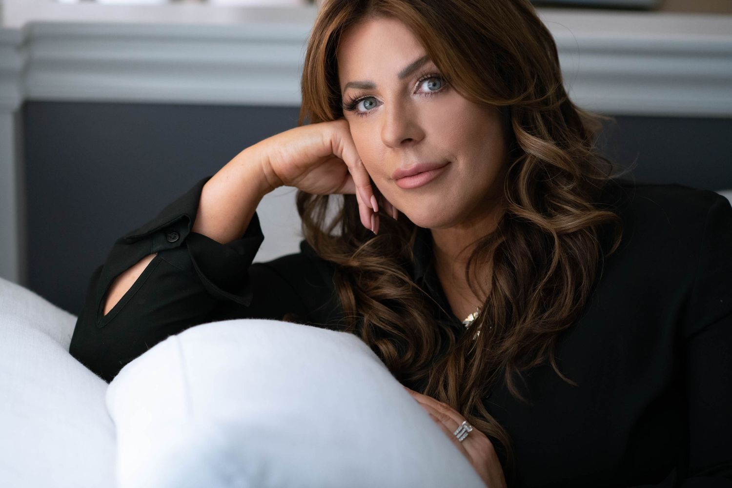 Relaxed portrait of woman in black top resting on couch in contemporary setting.