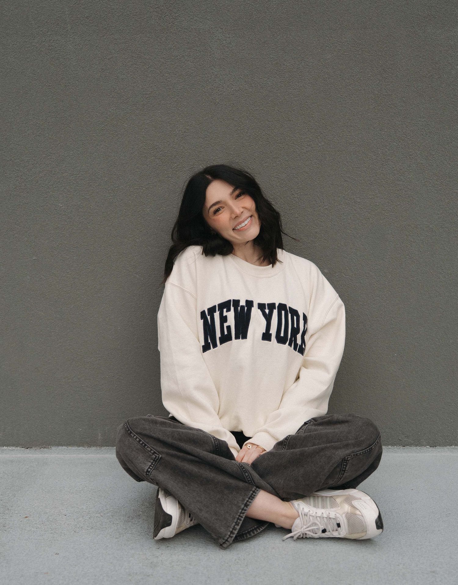 Person in New York sweatshirt poses casually against grey wall in multiple shots.