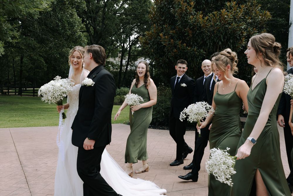 Wedding party walking together outdoors with bridesmaids in olive green dresses and carrying white bouquets.