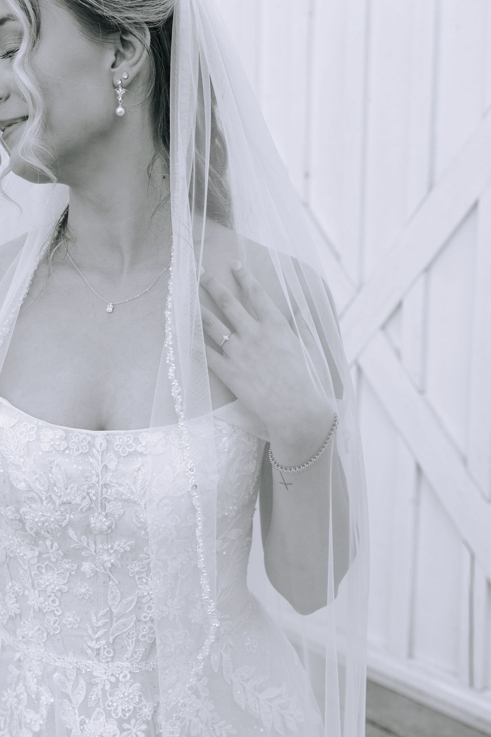 Close-up detail of bride's lace dress, veil, and delicate jewelry against white backdrop.