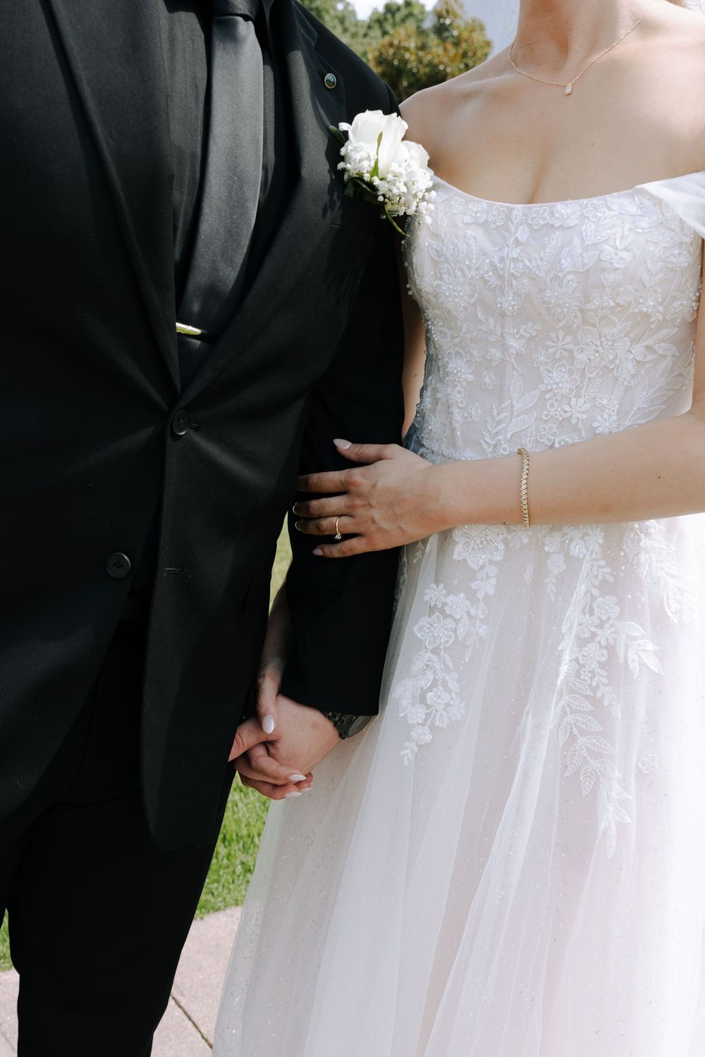 Close-up of newlyweds in formal attire showing details of white lace wedding dress and black suit.