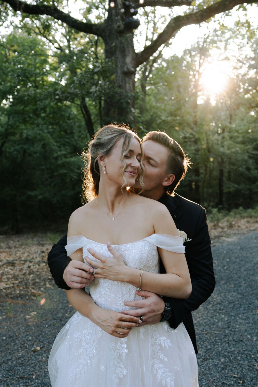 A romantic couple in formal wedding attire embraces outdoors during a sunset photo session.