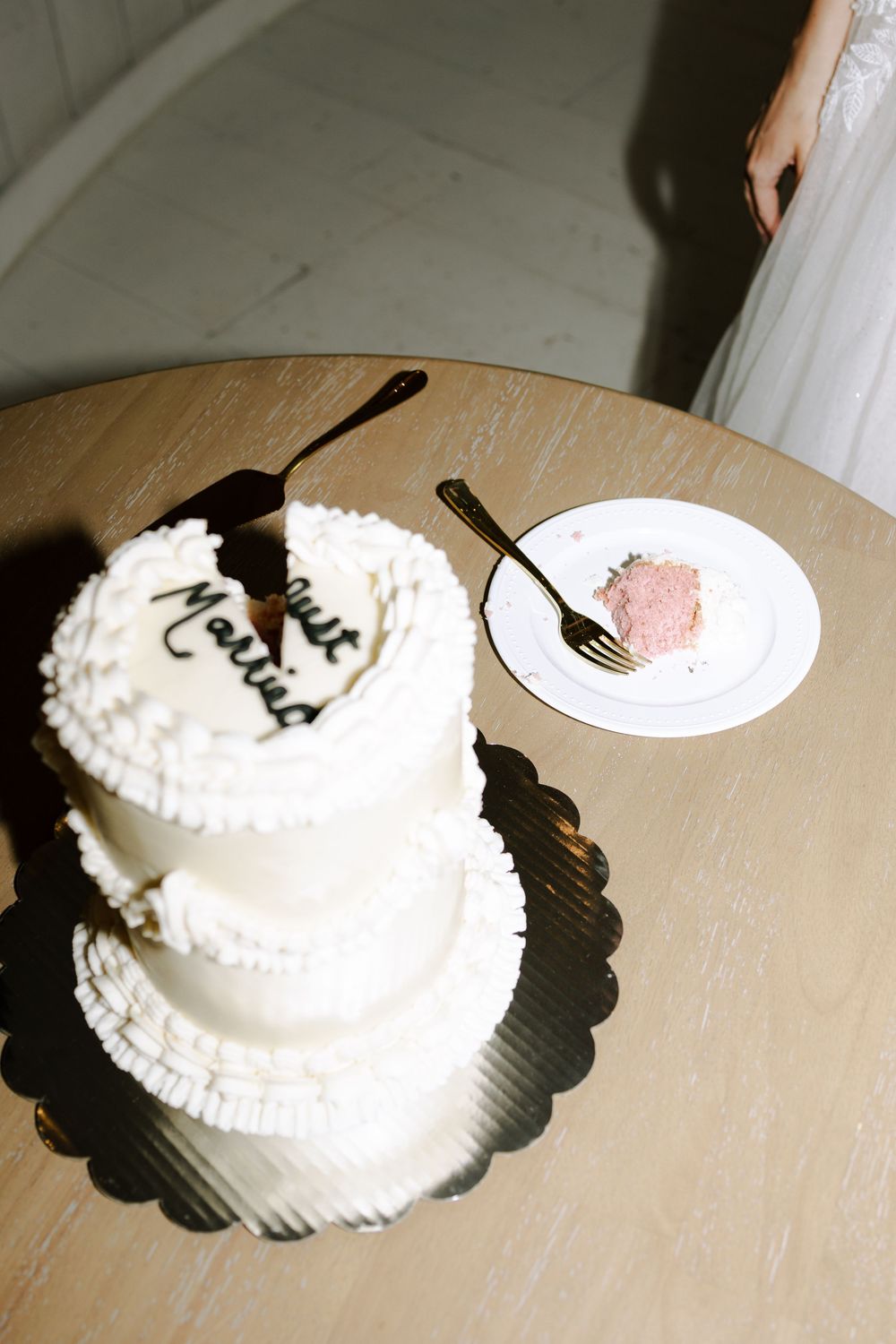 A three-tiered white wedding cake and a small plate with a slice of pink cake on a wooden table.