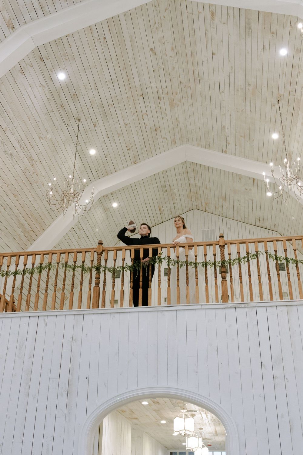 A church interior balcony with white wooden beams and chandeliers hanging from a vaulted ceiling.