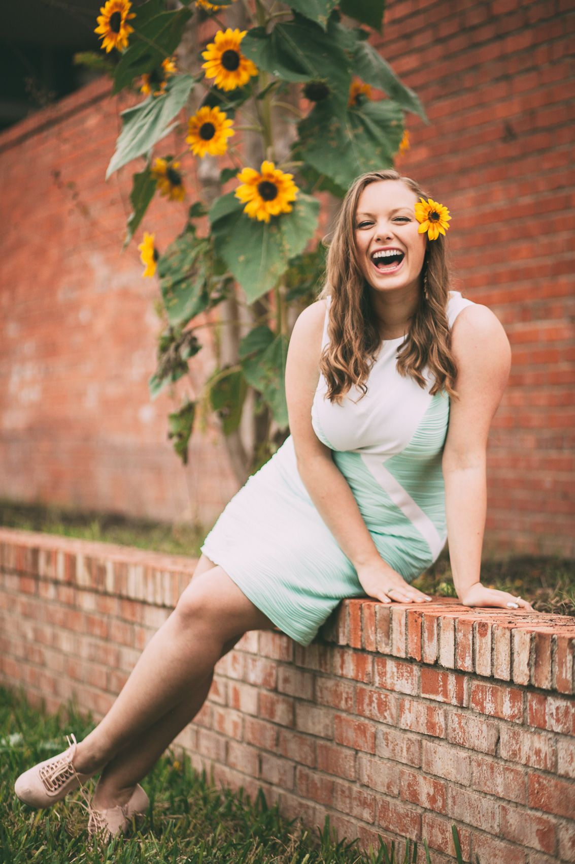 Joyful portrait with sunflowers against a brick wall in a mint green summer dress.