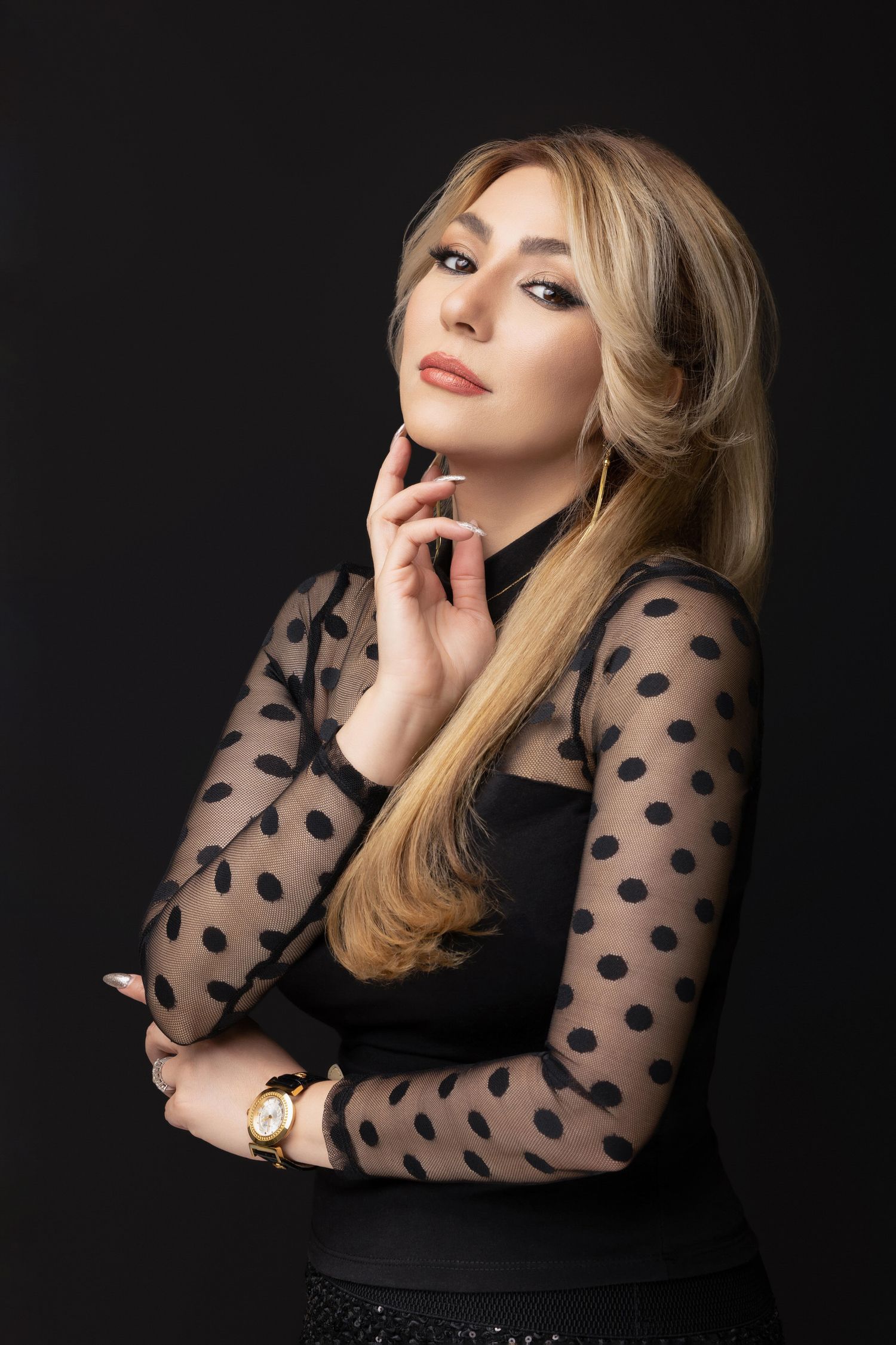 Studio portrait of a model wearing a black polka dot sheer-sleeved top against a dark background.