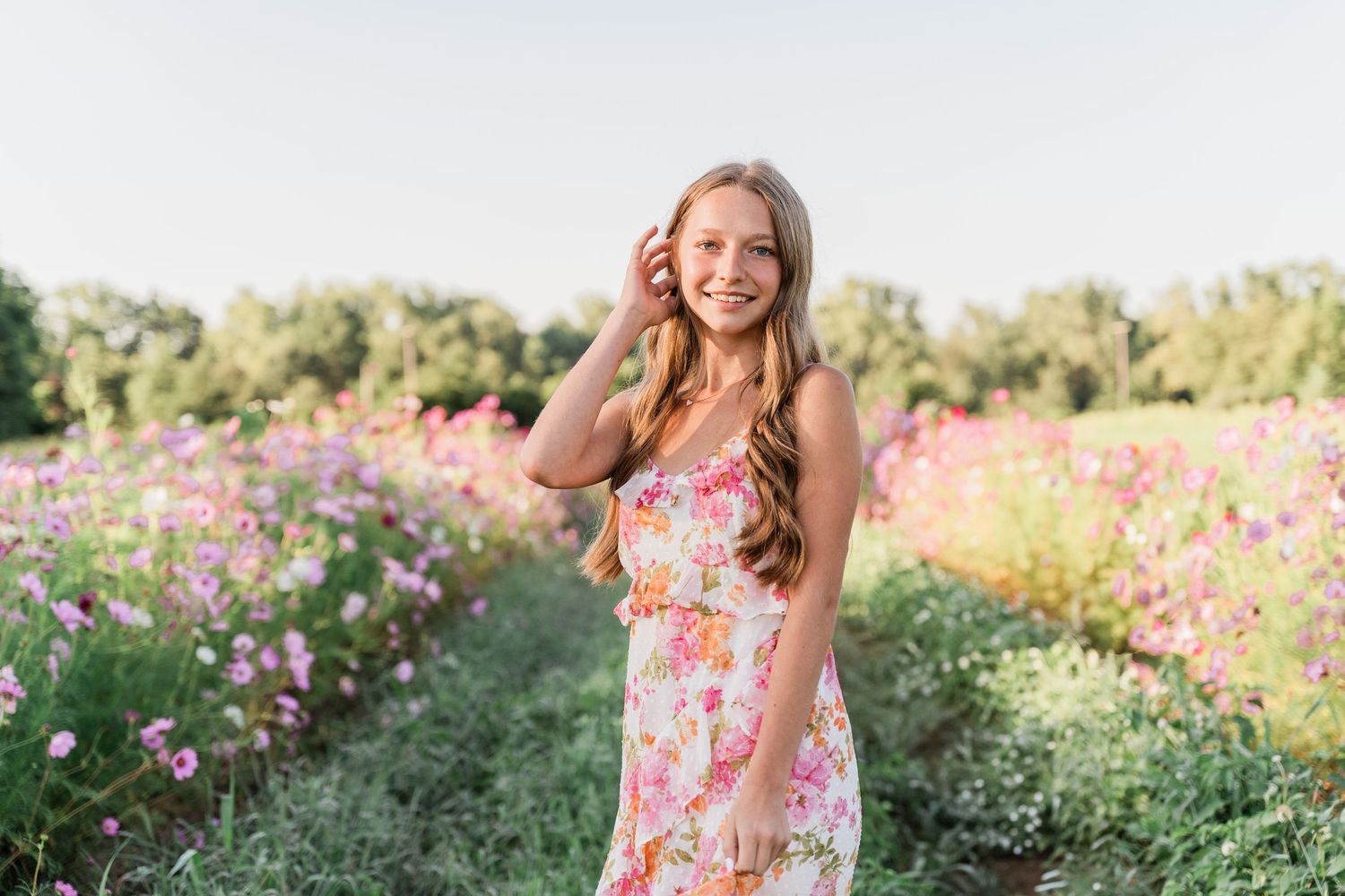 A Perrysburg senior photoshoot depicts girl in a colorful floral sundress posing naturally among blooming wildflowers in a meadow.
