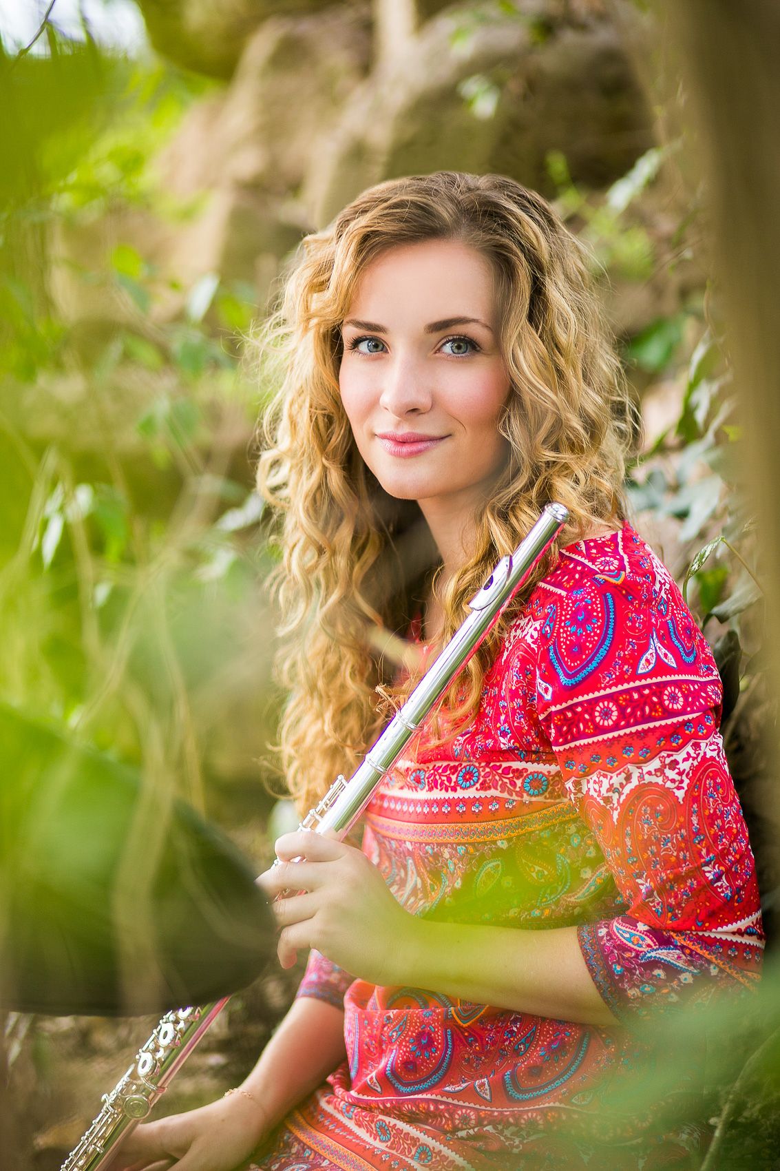 Portrait of a musician with a flute wearing a vibrant pink paisley top in nature.