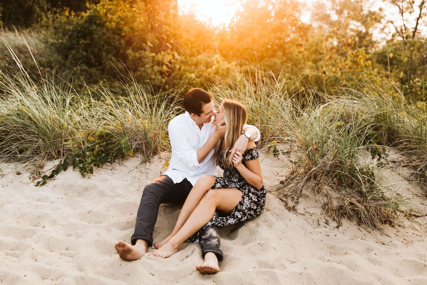 A couple sharing a romantic moment on sandy dunes during golden hour sunset.