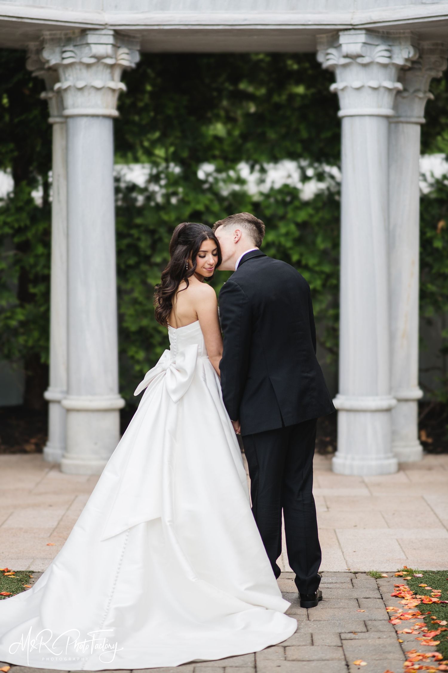Bride and groom share an intimate moment, foreheads nearly touching, before grand white marble columns.